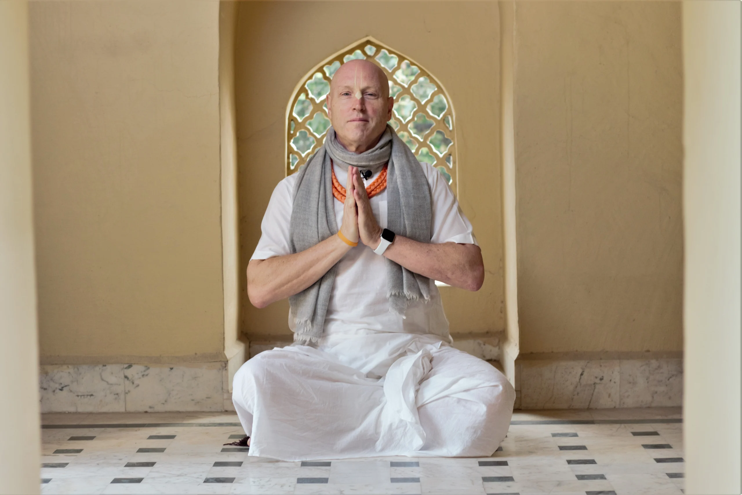 His Grace Vaiśeṣika Dāsa, smiling in a white kurta with tilak at a temple